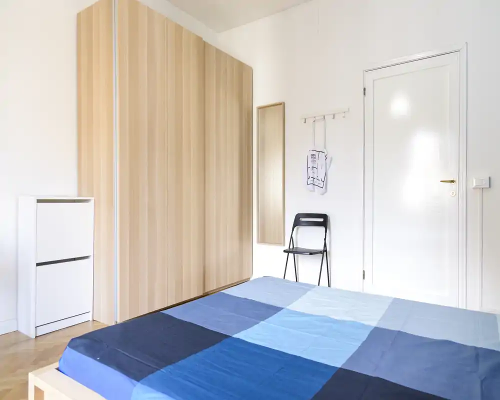 Chambre lumineuse et minimaliste avec un grand lit au premier plan, une armoire en bois clair et une décoration sobre — aérée et épurée.