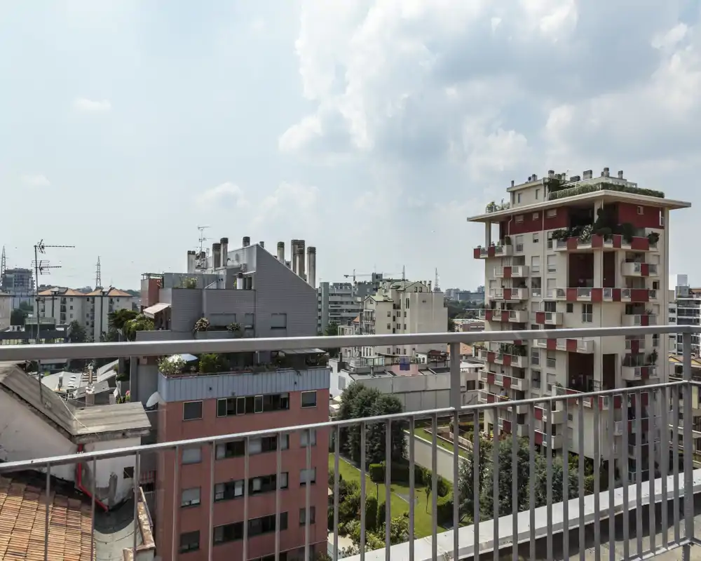 Sunny balcony view overlooking neighboring apartment buildings and a small green courtyard — ideal to showcase an urban terrace with railings and open sky.