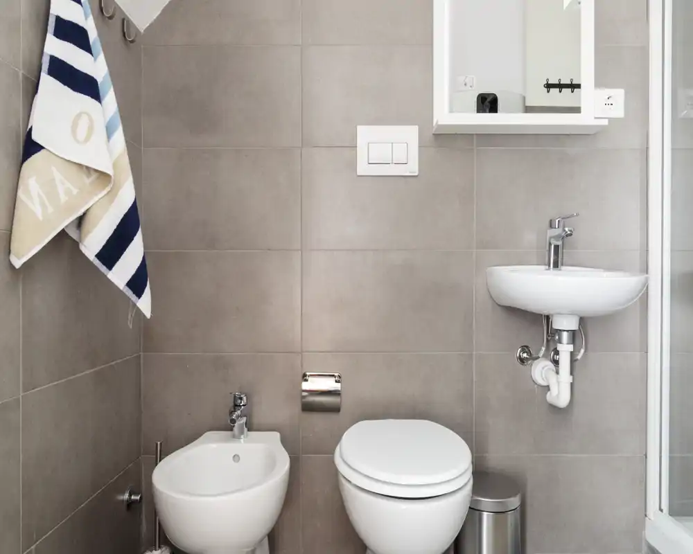 Compact, modern bathroom with toilet, bidet, small sink and tiled walls. Clean and bright fixtures suitable for a rental listing.