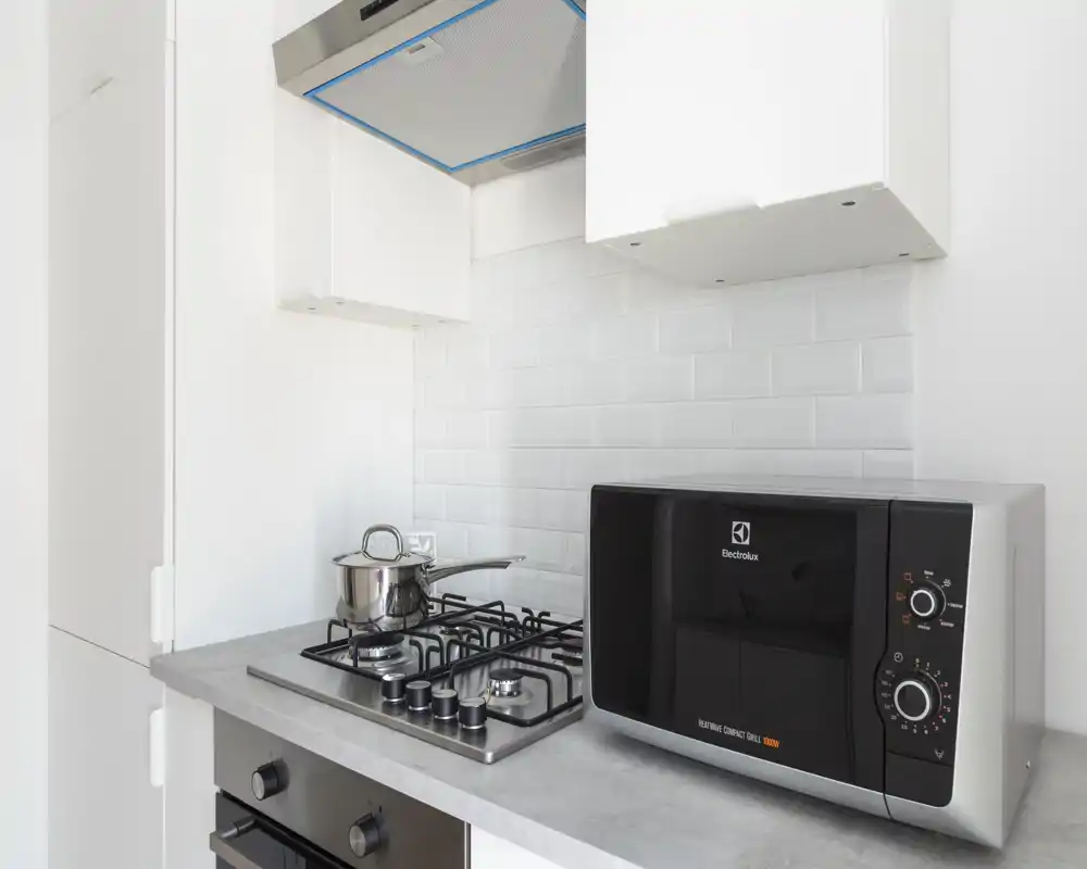 Bright, modern kitchenette with a gas hob, stainless saucepan and a compact microwave on a clean countertop — ideal for short-stay rentals.