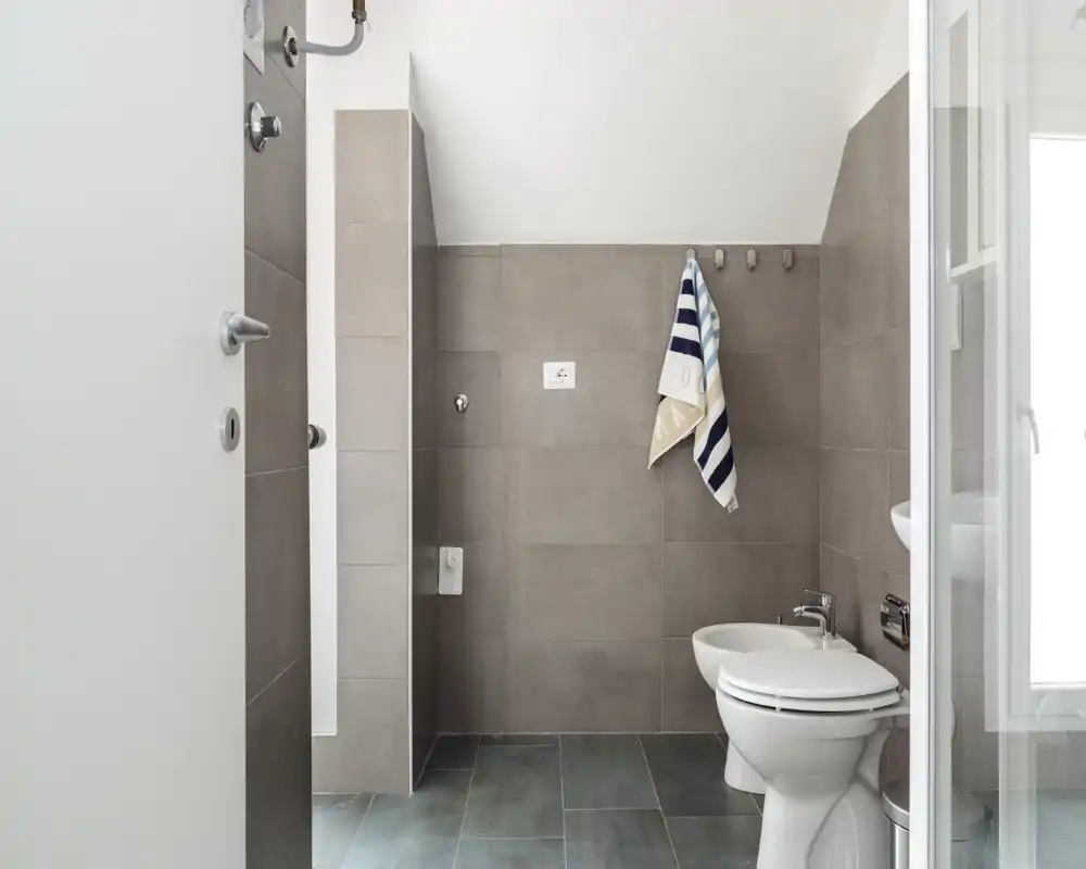 Clean, modern bathroom with wall-mounted tiles, toilet and bidet, and a towel hanging on hooks — bright, minimalist design.