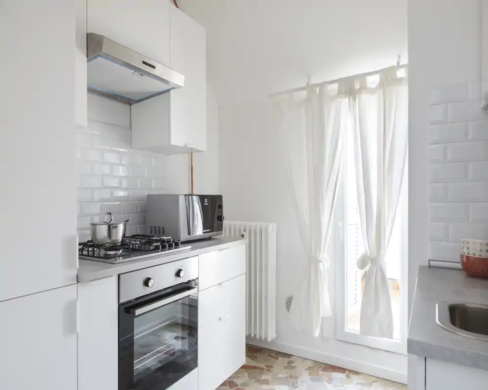 Bright modern kitchen with a gas hob, built-in oven, microwave and a sink area; white cabinets and tiled backsplash create a clean, minimalist look.