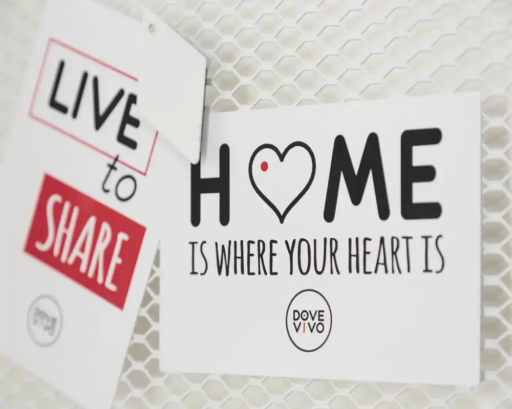 Close-up of decorative wall cards reading 'HOME is where your heart is' and 'LIVE to SHARE' on a mesh background. The photo focuses on signage and texture rather than any room layout or furniture.