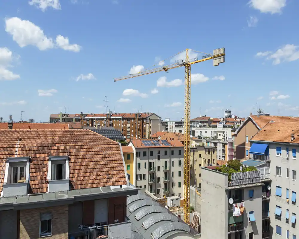 Rooftop city view showing neighboring apartment roofs, a construction crane and a clear blue sky — ideal to illustrate an urban balcony or terrace outlook.