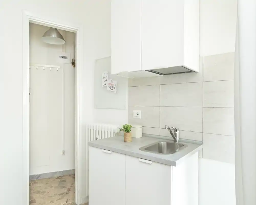 Compact modern kitchen corner with a stainless-steel sink, light grey countertop and white cabinets; bright, minimal and well organized — ideal for small apartments.