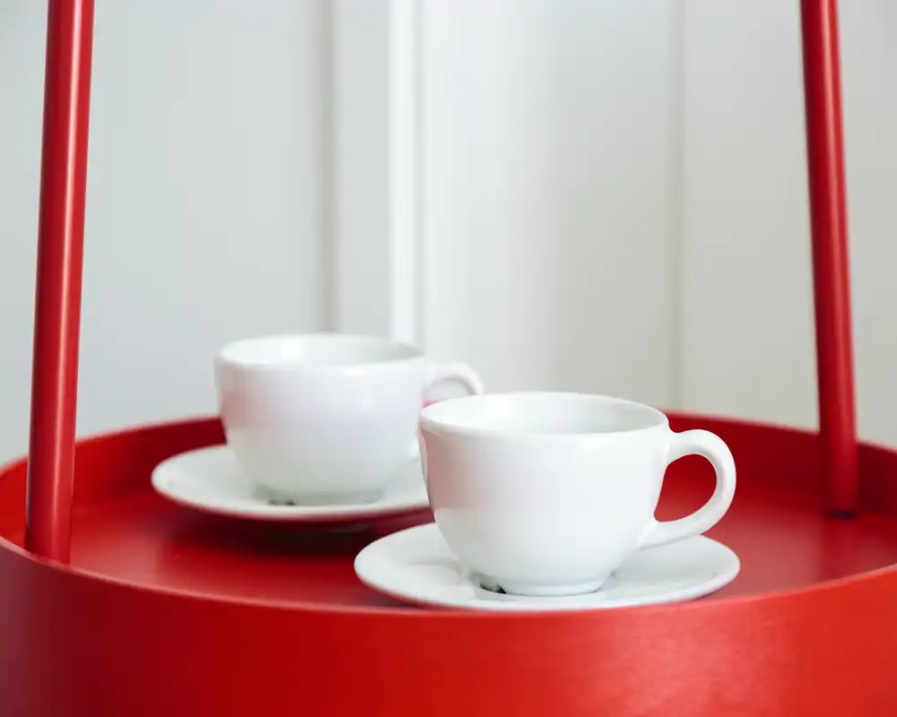 Close-up of two white coffee cups on a bright red serving tray; no room context is visible.