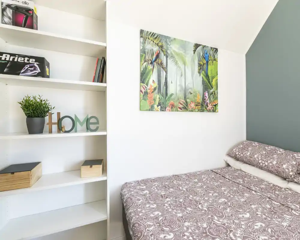 Chambre compacte et lumineuse avec literie à motifs, tableau décoratif et étagères intégrées — un lit accueillant, idéal pour courts séjours.
