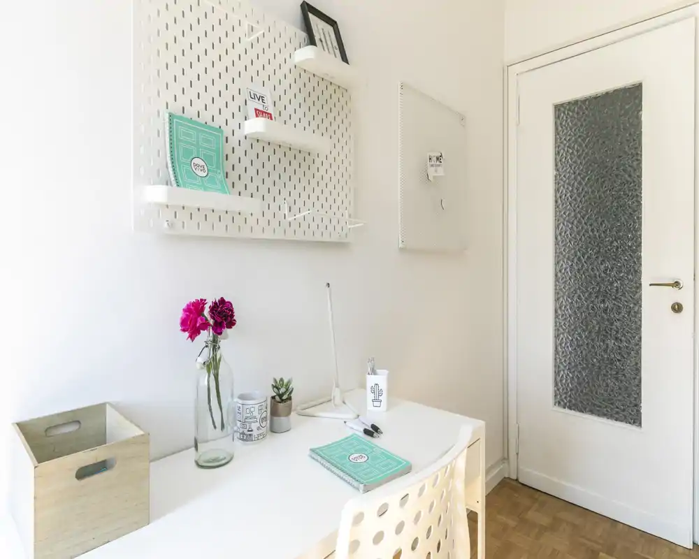 Coin bureau lumineux et minimaliste dans un séjour, avec un bureau blanc, des étagères décoratives et une porte en verre texturé — style moderne et épuré pour travailler.