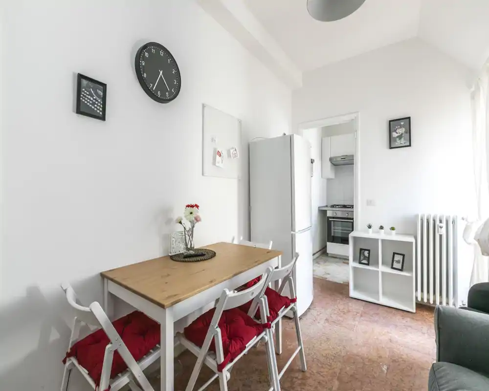 Coin cuisine-salle à manger compact et lumineux avec table en bois, quatre chaises aux coussins rouges, réfrigérateur visible et four dans l'entrée — idéal pour des repas conviviaux.