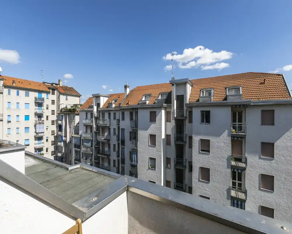 Balcon ensoleillé avec vue sur les toits des immeubles voisins et ciel bleu — parfait pour présenter une terrasse extérieure ou un petit balcon.