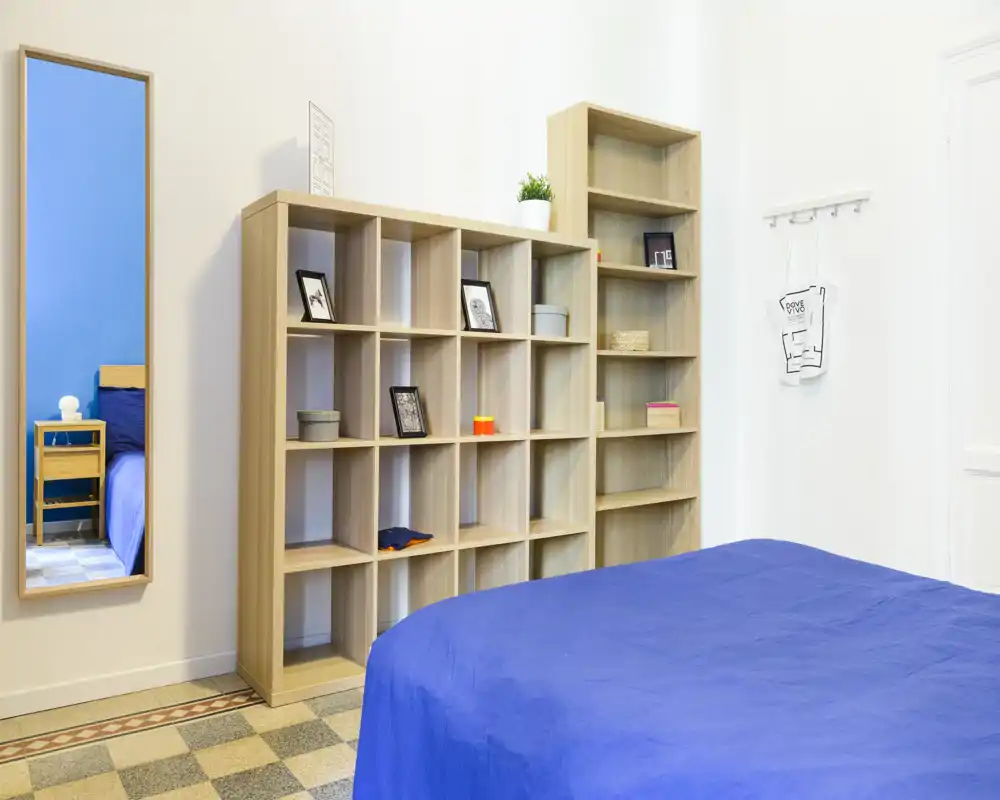 Chambre lumineuse et moderne avec couvre-lit bleu, étagères ouvertes et miroir pleine longueur ; espace minimaliste et bien éclairé, parfait pour les annonces.