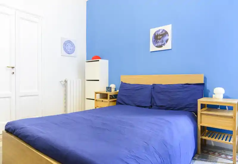 Chambre lumineuse et soignée avec un lit double devant un mur bleu vif, tables de chevet en bois et de petites touches décoratives — idéale pour les annonces.