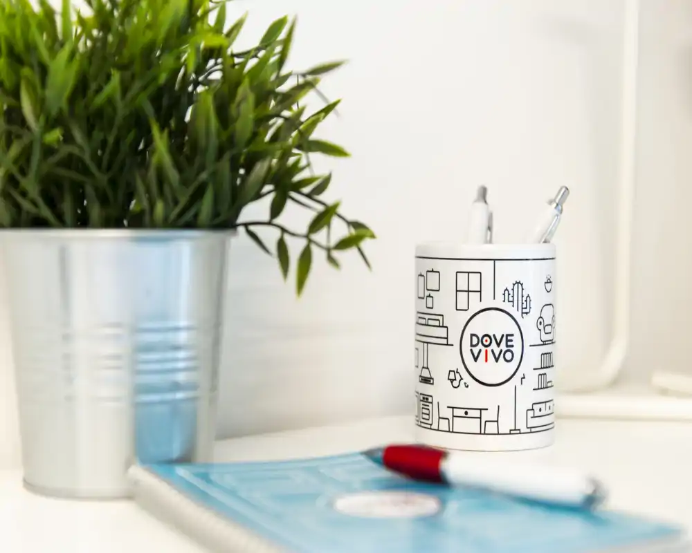 Gros plan d’un coin de bureau soigné avec une petite plante en pot, un porte-stylo marqué contenant des stylos et un carnet — une image d’ambiance parfaite pour illustrer des détails ou des équipements.