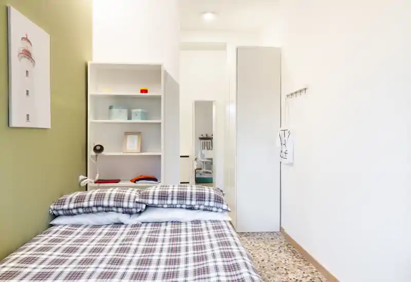 Chambre lumineuse et bien rangée avec lit à motifs au premier plan, étagères ouvertes et rangement minimaliste — idéale pour un séjour confortable.