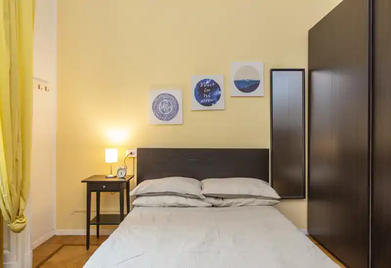 Well-staged bedroom with a double bed, bedside table and warm lighting; neutral linens and framed wall art create a cozy, inviting atmosphere ideal for rental photos.