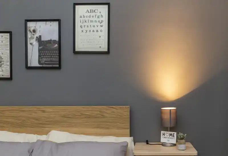 Angolo camera da letto luminoso e stiloso con testiera in legno, quadri appesi e una calda lampada da comodino che crea un'atmosfera accogliente.