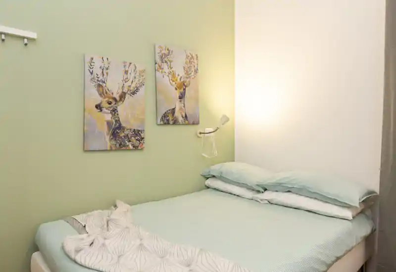 Dormitorio acogedor y bien iluminado con cama doble vestida con ropa de cama color menta y cuadros decorativos de ciervos en una pared verde claro.