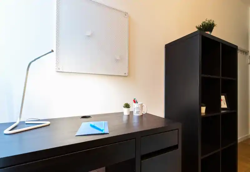 Rincón de trabajo luminoso y minimalista con escritorio de madera oscura, lámpara moderna, pequeñas plantas y estantería modular — ideal para concentrarse o estudiar.