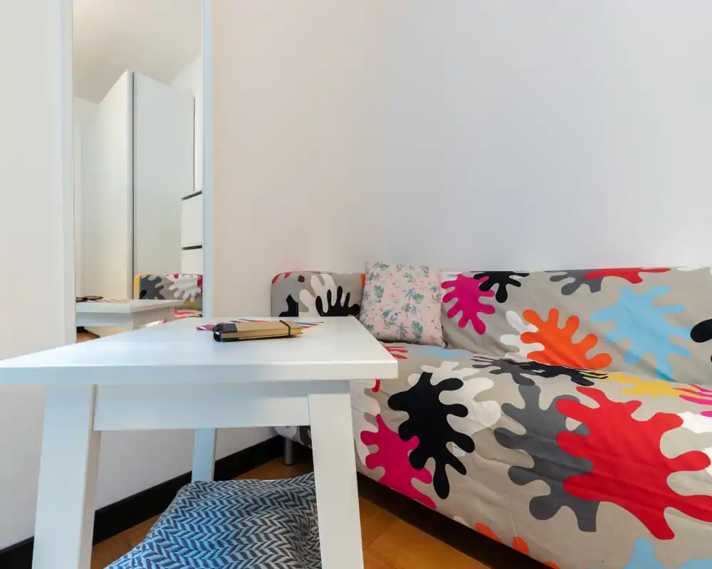 Zona de estar compacta y luminosa con un sofá colorido y una pequeña mesa blanca — ideal para un rincón acogedor.