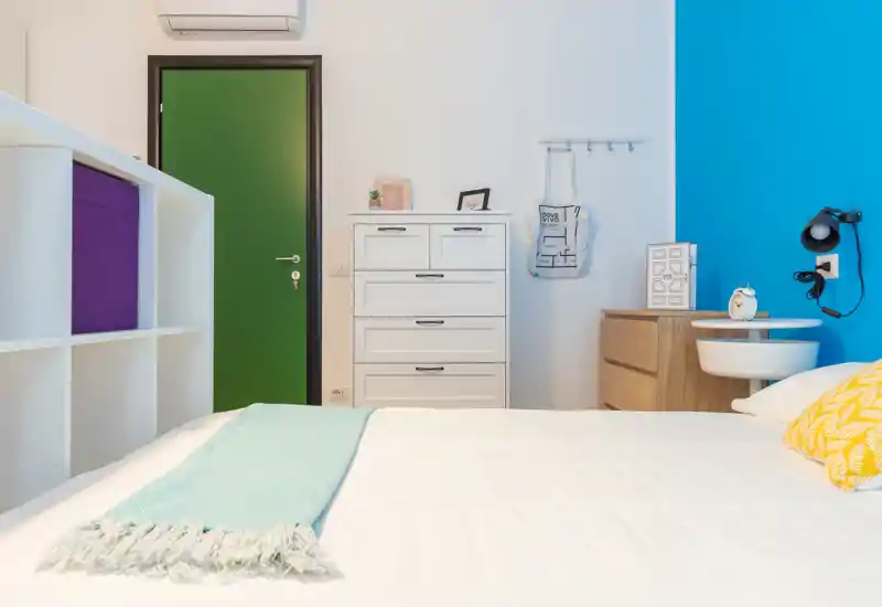 Dormitorio moderno y luminoso con una cama grande en primer plano, pared de acento colorida y almacenaje ordenado, perfecto para alquileres vacacionales.
