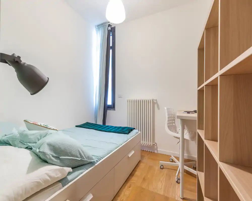 Bright, modern single bedroom with a neatly made bed, minimalist shelving and a small desk by the window — ideal for a student or single renter.