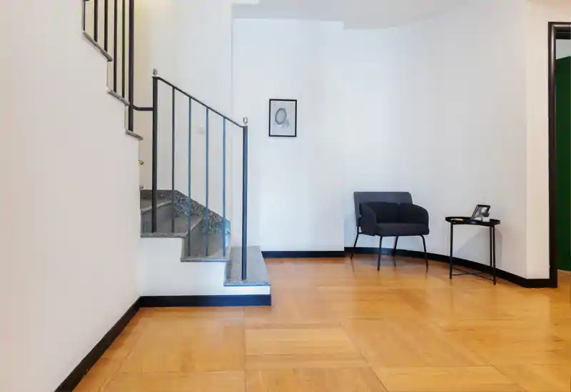 Entrada luminosa y minimalista con una pequeña escalera, un sillón y una mesita auxiliar — suelos de madera cálida y líneas limpias que transmiten una bienvenida acogedora.