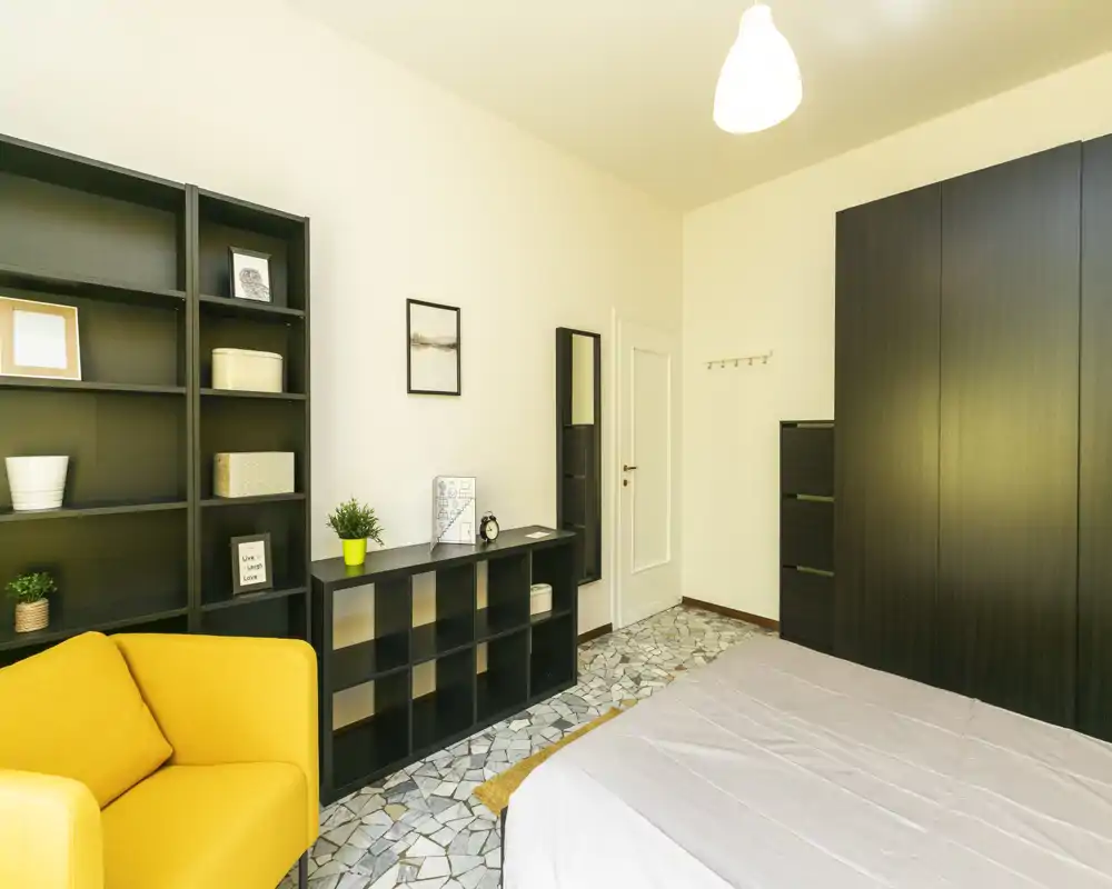 Chambre moderne et lumineuse avec grand dressing, étagères et un fauteuil jaune chaleureux ; la pièce est bien éclairée et le lit est clairement visible.