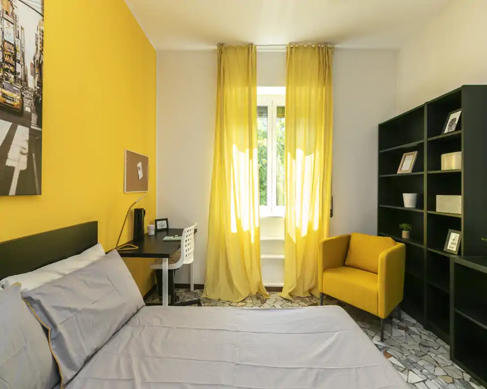 Chambre lumineuse et bien aménagée avec lit double, petit bureau, rideaux jaunes et fauteuil assorti — espace accueillant idéal pour la location.