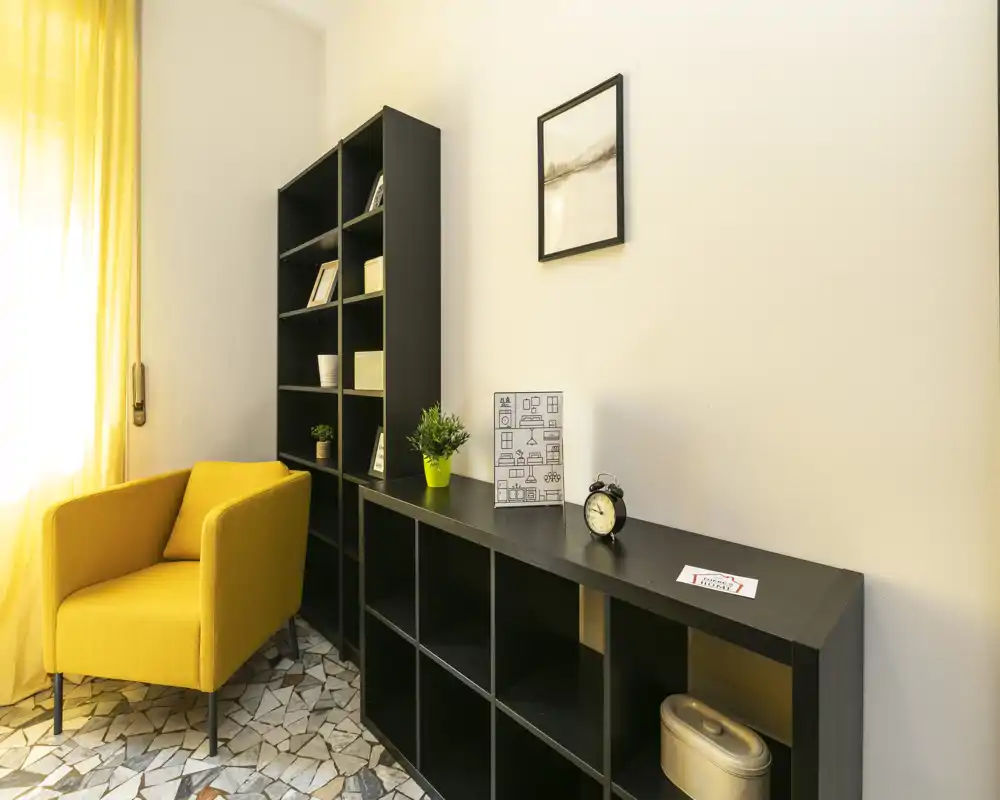 Coin salon lumineux et stylé avec un fauteuil jaune, des étagères noires et des éléments décoratifs — idéal pour la lecture et la détente.