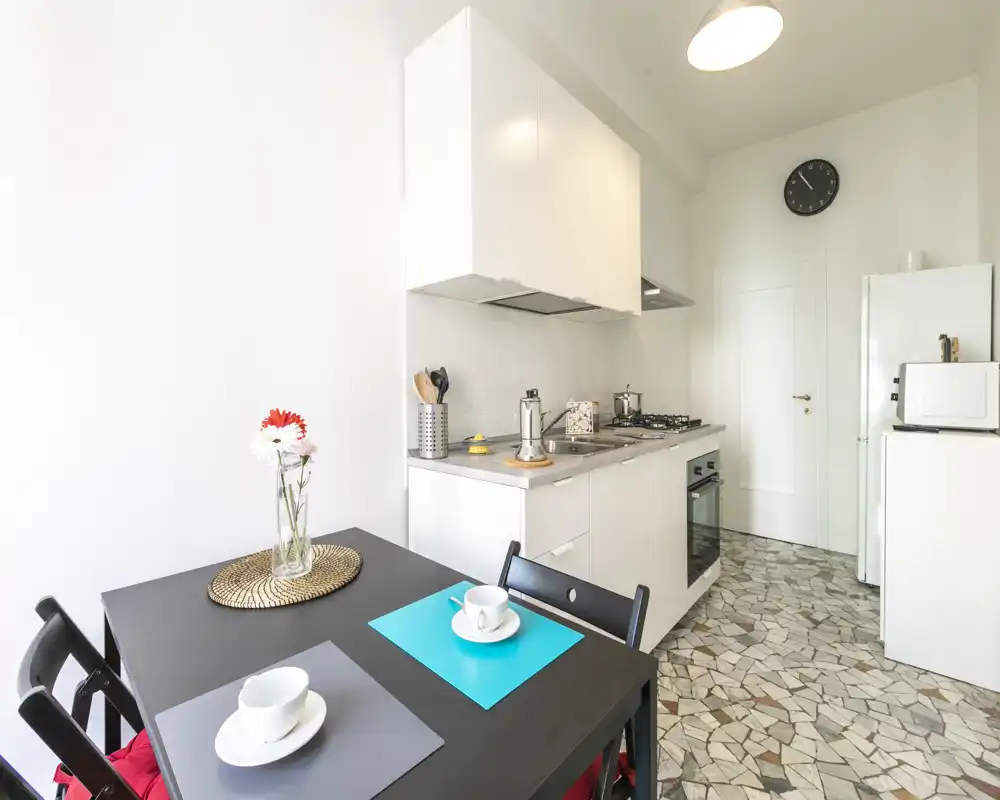 Kitchenette lumineuse et moderne avec meubles blancs, plaques à gaz et petite table pour deux — parfaite pour un séjour en ville.