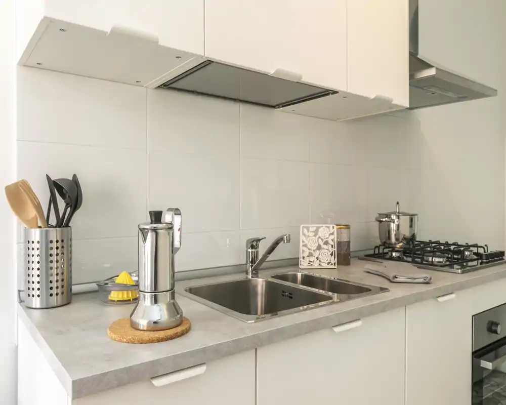 Plan de travail de cuisine moderne et lumineux avec évier en acier, plaque à gaz et petits appareils ; propre, fonctionnel et bien éclairé.
