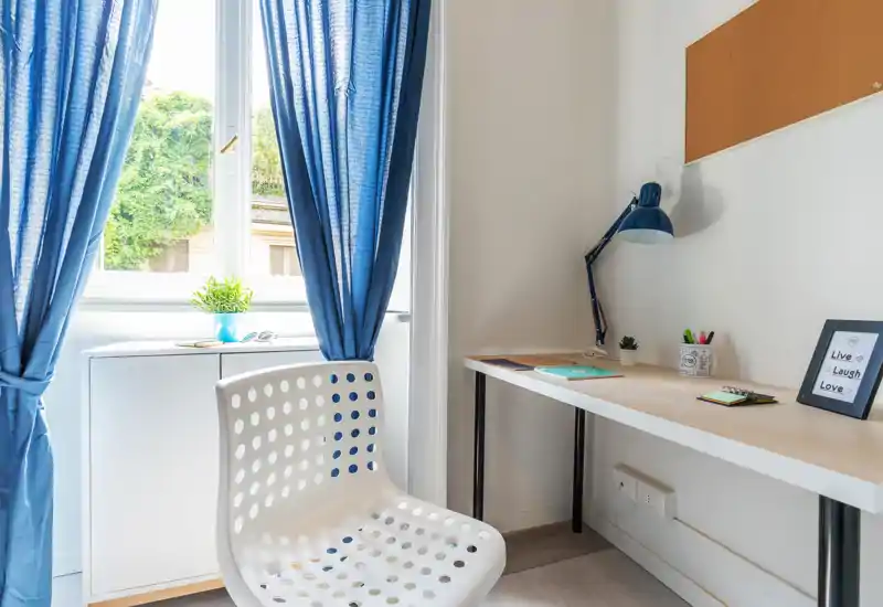 Rincón de estudio luminoso y minimalista con silla blanca perforada, lámpara de escritorio, pequeña planta y luz natural desde la ventana — ideal para concentrarse.