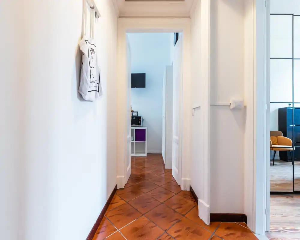 Bright, clean hallway with terracotta floor tiles, white walls and a doorway leading to other rooms; suitable for showing the apartment entrance and circulation space.