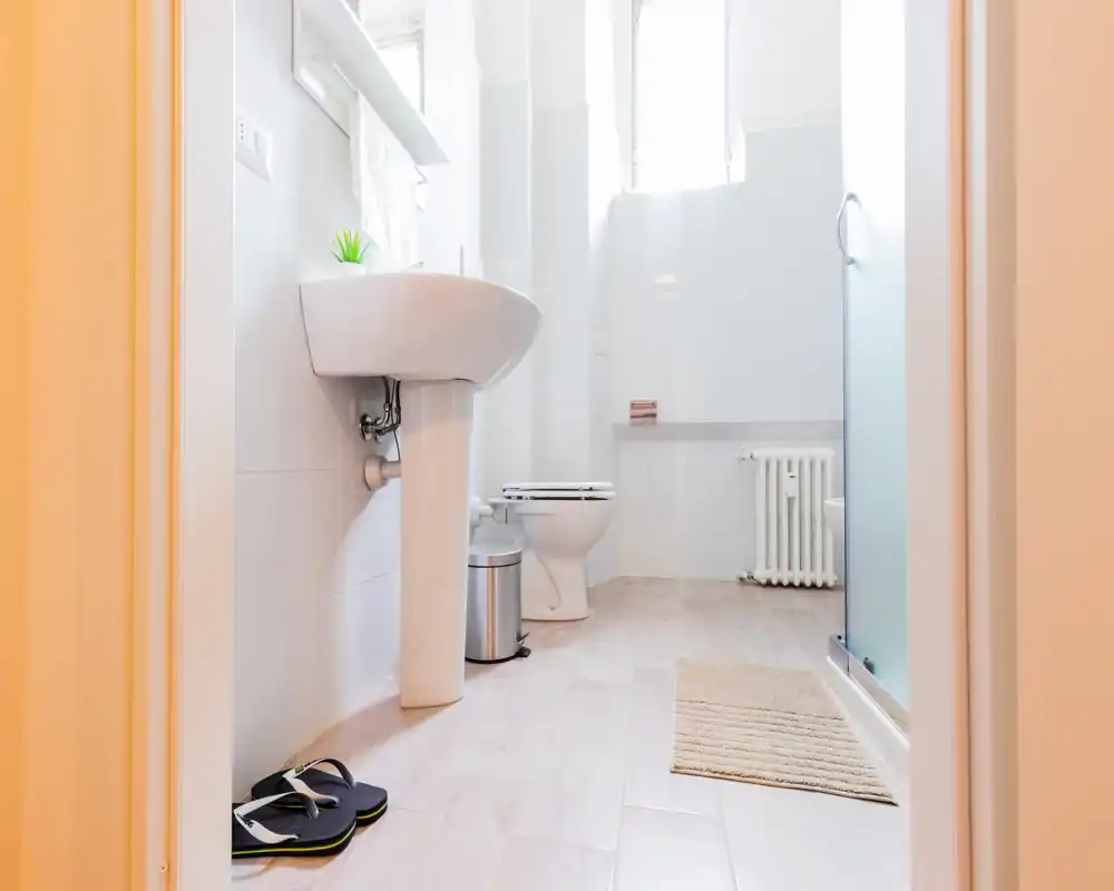 Bright, clean bathroom with pedestal sink, toilet, glass shower and light wood-effect flooring — ideal for rental listings highlighting modern, fresh sanitary spaces.