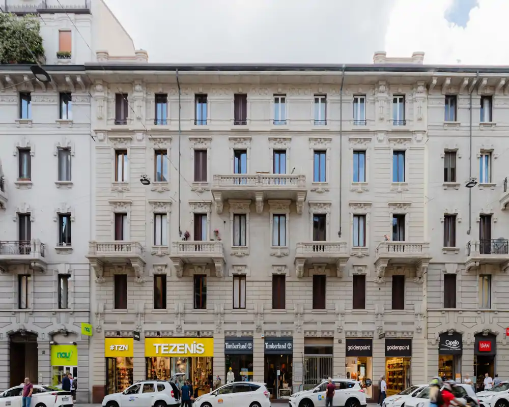 Street-level view of a classic multi-story city building with retail shops on the ground floor; architectural details and balconies are clearly visible.