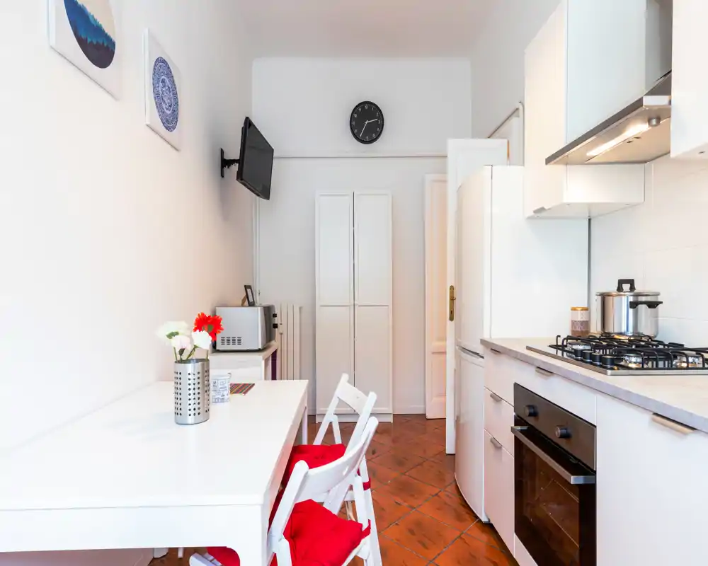 Bright, compact kitchen with modern appliances, a gas hob and built-in oven, plus a small dining table with red-cushioned chairs—ideal for a cozy city apartment.