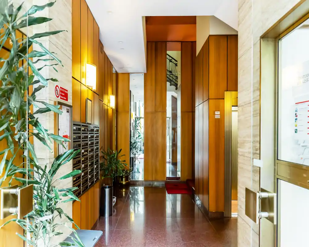 Well-lit building entrance with wood-paneled walls, mailboxes and potted plants; polished floor and a glass door provide a tidy, welcoming first impression.