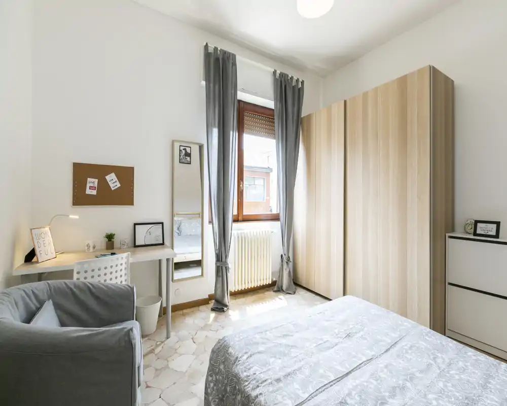 Camera da letto luminosa e moderna con ampio armadio, letto matrimoniale comodo e una piccola scrivania vicino alla finestra — toni neutri e luce naturale per un’atmosfera rilassante.