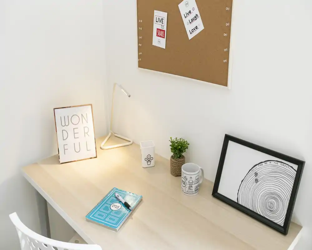 Angolo studio luminoso e minimal con scrivania in legno, lampada da tavolo, piccoli oggetti decorativi e bacheca in sughero — perfetto per lavoro o studio.