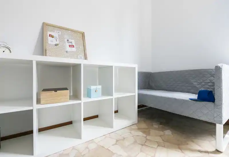 Minimal, bright living area with a modern grey upholstered sofa and white cube shelving, styled in a clean, airy layout — ideal for compact apartments.