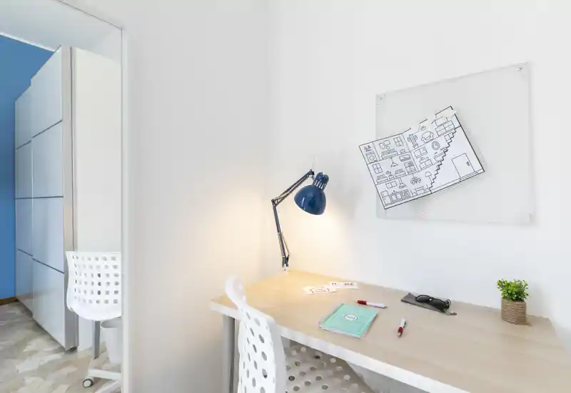 Neat study corner with a light wood desk, task lamp and perforated white chair — a bright, well-lit workspace with small decorative touches.