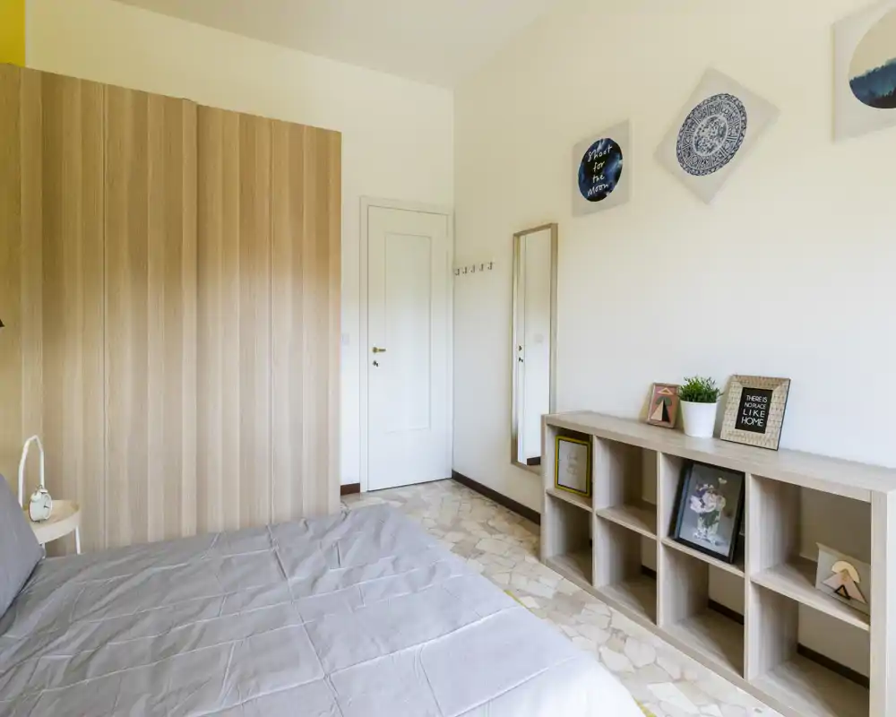 Chambre lumineuse et moderne avec un lit double bien fait, des rangements en bois et un grand miroir, style épuré et minimal idéal pour une annonce.