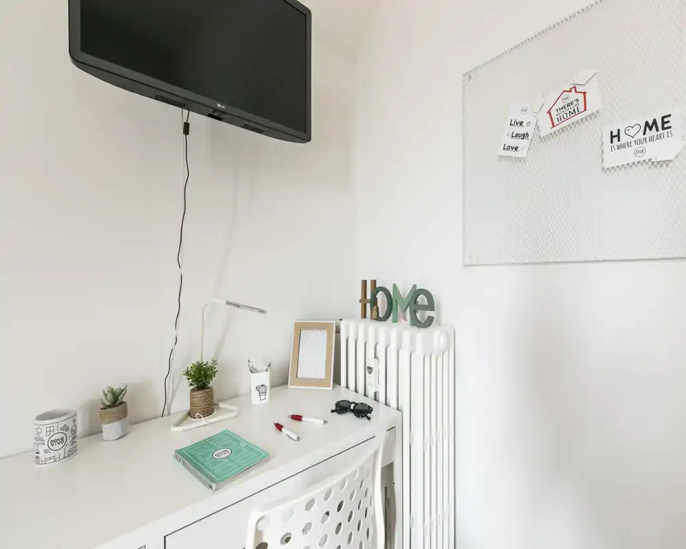 Angolo scrivania luminoso e minimal con elementi decorativi e TV a muro — ideale per lavorare o studiare in uno spazio moderno e accogliente.
