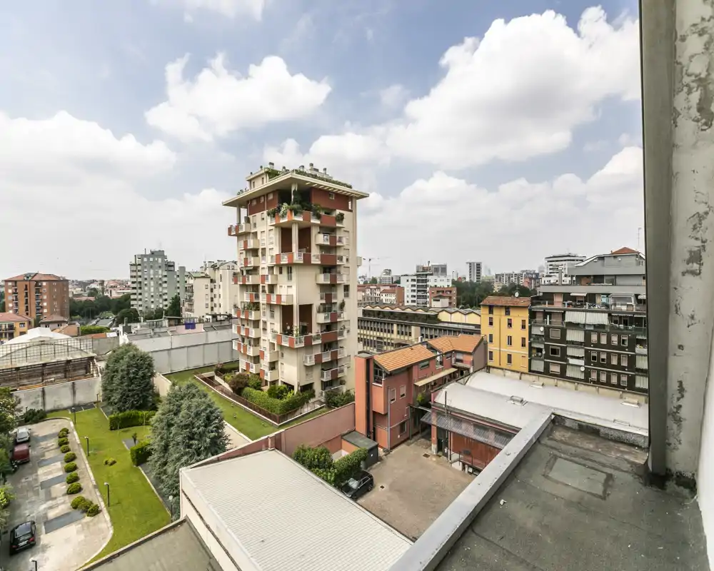 Vista urbana luminosa da balcone/terrazzo con edifici residenziali e cortili curati, ideale per mettere in evidenza l’aspetto esterno dell’immobile.