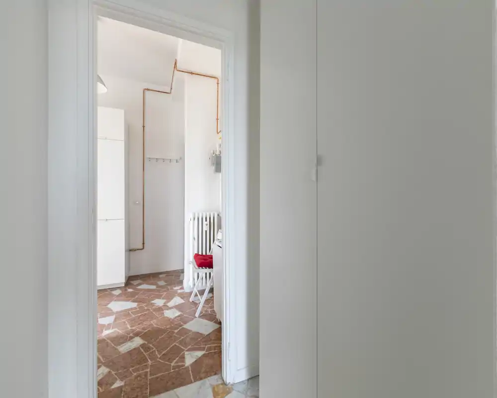 Vista attraverso una porta su un piccolo ingresso/area di servizio con pavimento a piastrelle, radiatore e armadio; spazio neutro e luminoso adatto all'ingresso.