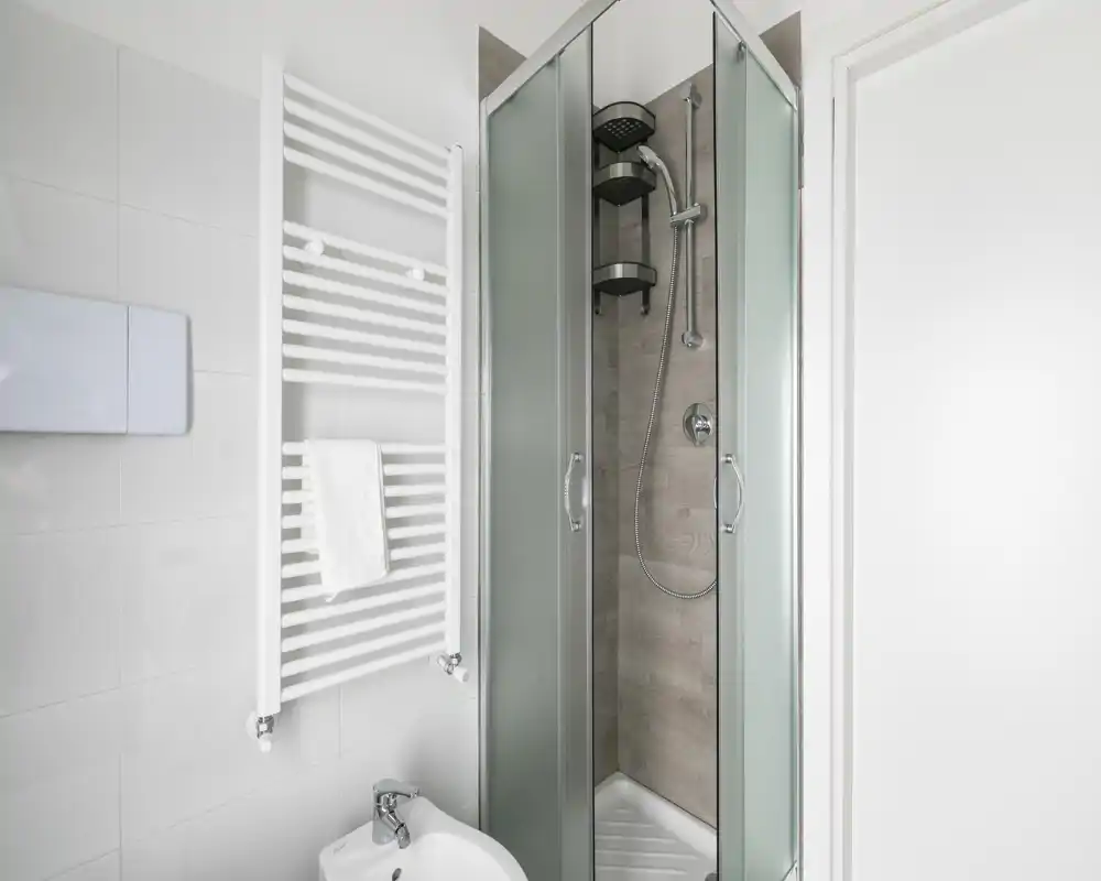 Bagno moderno e compatto con cabina doccia angolare con porte in vetro smerigliato, scaldasalviette a parete e bidet; luminoso, pulito e funzionale.