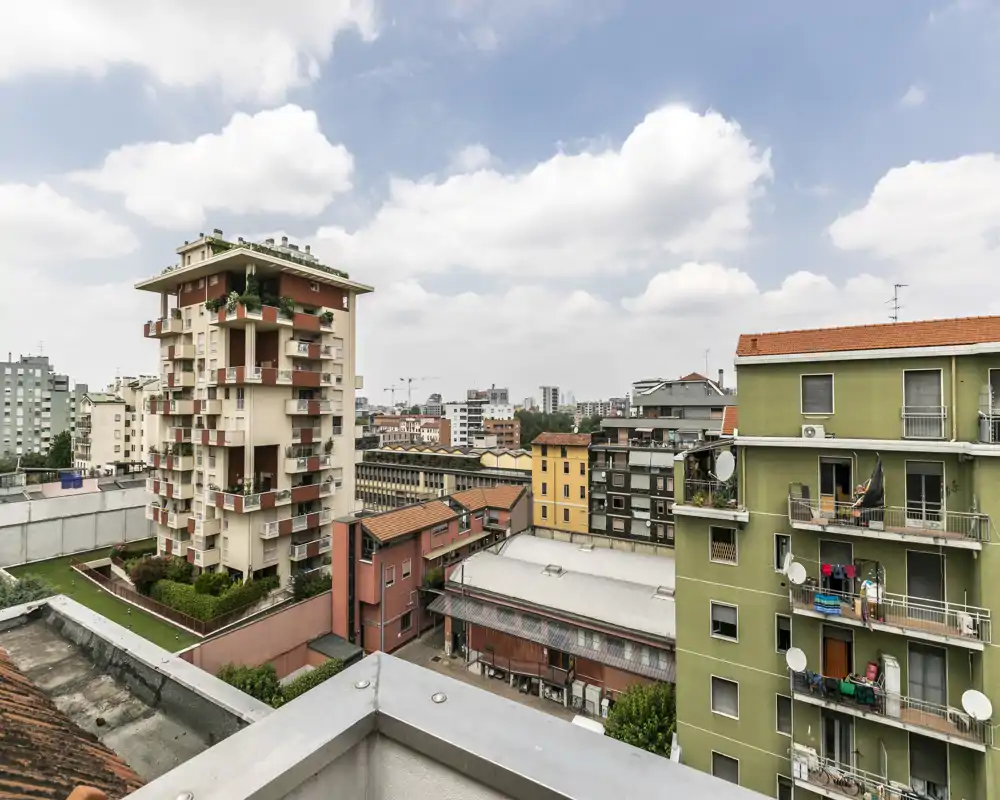 Vista cittadina da un balcone/terrazza al piano alto con edifici vicini, tetti e un ampio cielo nuvoloso — perfetta per mostrare la posizione e il panorama.