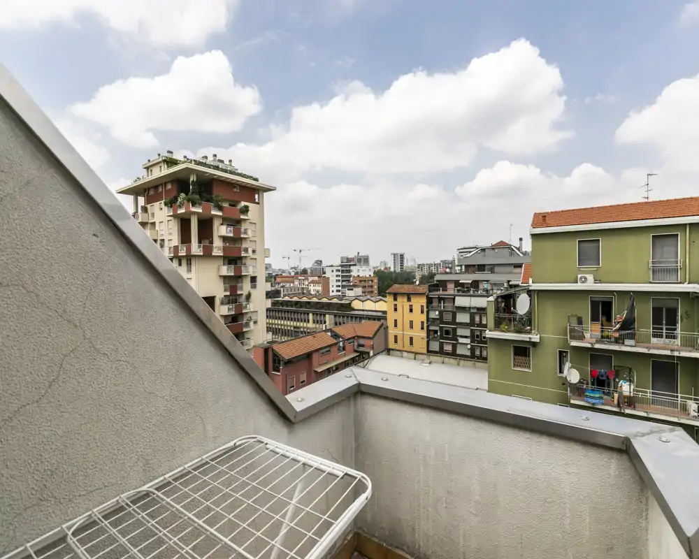 Piccolo balcone urbano con vista sui palazzi vicini e cielo parzialmente nuvoloso, adatto per stendere i panni o prendere aria fresca.