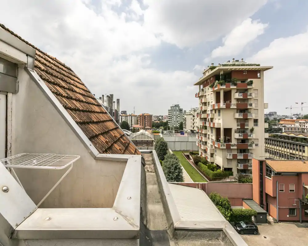 Vista dalla terrazza sul tetto verso gli edifici residenziali vicini, con dettagli delle tegole e uno skyline cittadino aperto.