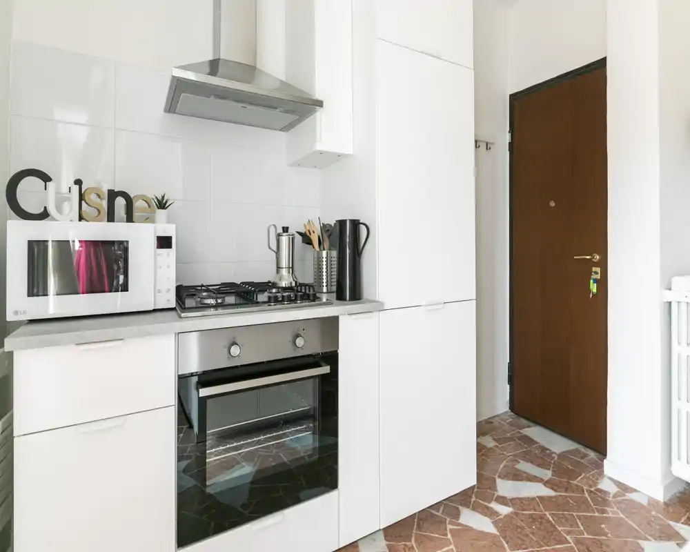 Cucina moderna compatta con mobili bianchi, forno incassato e piano cottura a gas, microonde e cappa; luminosa e curata, ideale per annunci.